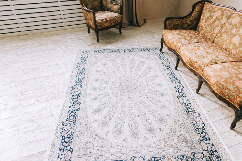 A patterned area rug is placed on a light wooden floor, with an ornate sofa and armchair in the background.