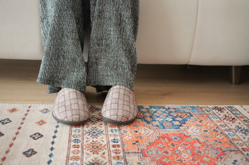Person wearing striped pants and plaid slippers sits on a light-colored sofa with their feet on a patterned rug.